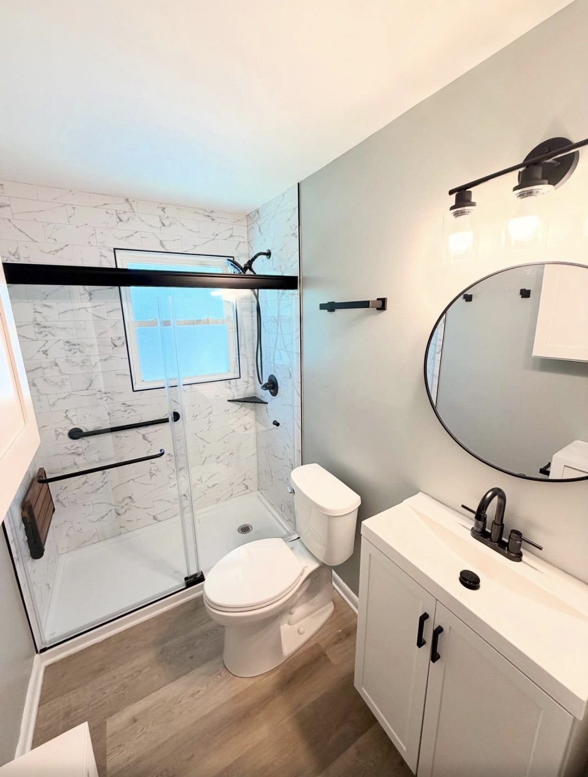 Remodeled bathroom with a marble-look tile shower, glass doors, new vanity and black fixtures.