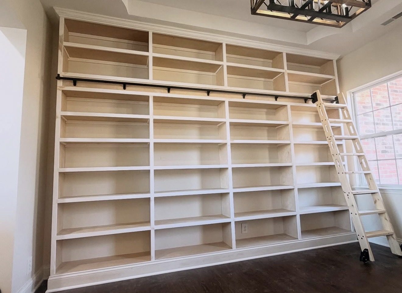 Floor-to-ceiling white built-in bookshelves with a rolling library ladder, built by Uncapher Co.