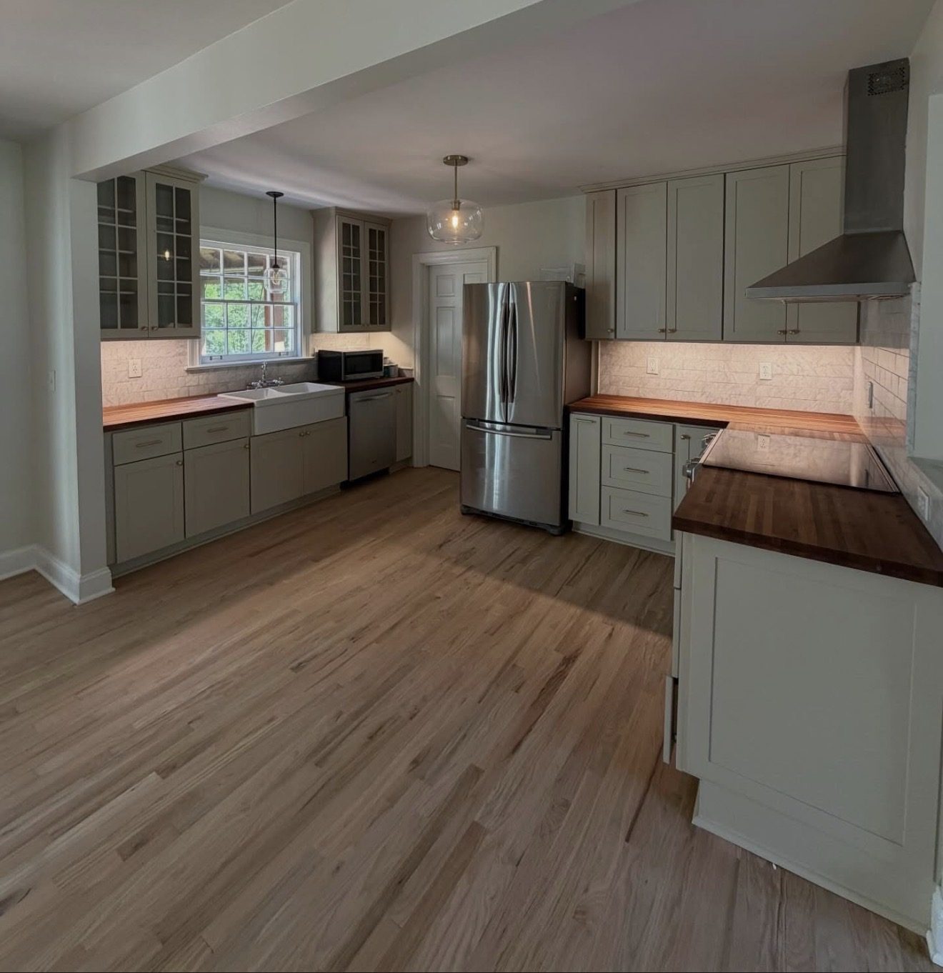 Kitchen with sage green cabinets, butcher block counters, farmhouse sink, and glass upper doors.
